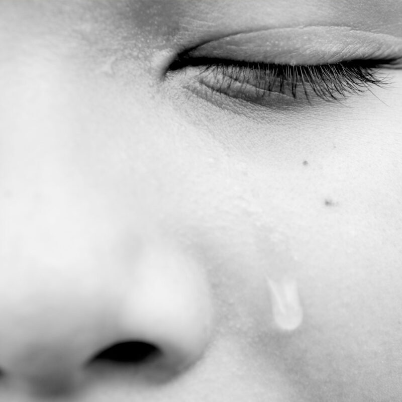 A close-up black-and-white image of a person’s closed eye with a tear on their cheek.